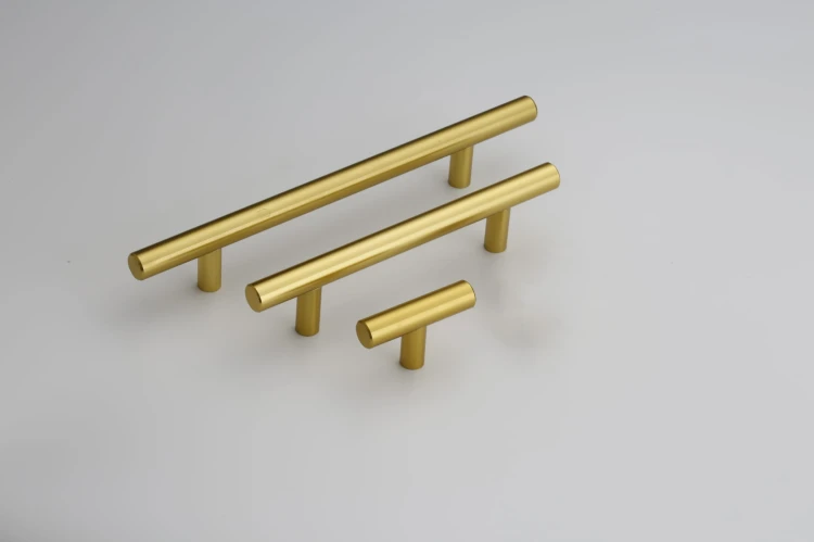 Längliche gebürstete goldene Uno-Möbelgriffe im T-Bar-Design, in einer Reihe auf hellem Hintergrund angeordnet