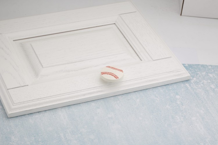 Möbelknopf in Baseballform, montiert an einer weißen Schubladenfront.